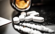 A detailed view of fentanyl pills and white powder on a reflective surface, illustrating the opioid crisis and prescription drug misuse. Subtle reflections and contemporary elements enhance the scene.